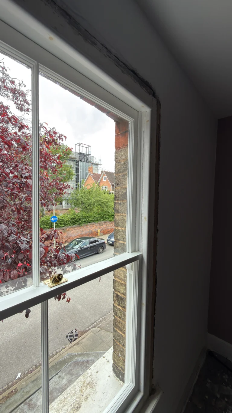 Sash window mid-restoration with a newly fitted brass fastener and stripped timber frame, on a period property near Bedford.